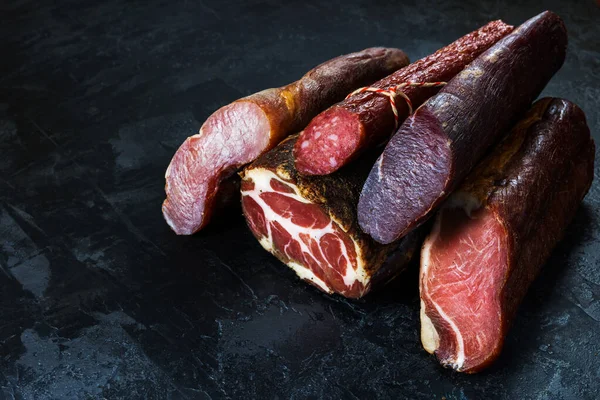 Jambon, sosis, jambon, jambon, siyah arka planda pastırma. Etli meze, pankart, menü. Boşluğu kopyala.