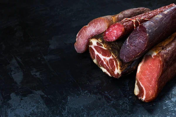 Jambon, sosis, jambon, jambon, siyah arka planda pastırma. Etli meze, pankart, menü. Boşluğu kopyala.