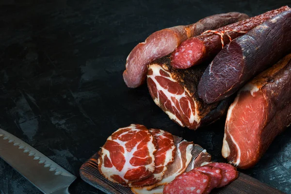 Jambon, sosis, jambon, jambon, siyah arka planda pastırma. Etli meze, pankart, menü. Boşluğu kopyala.