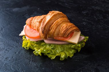 Kahvaltıda taze kruvasan sandviçi jambon ve siyah tabakta peynir.