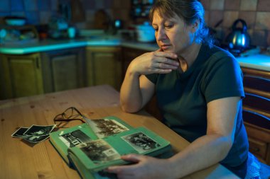 Orta yaşlı bir kadın aile albümüne bakıyor. Nostalji, üzüntü, keder ve anılar orta yaş kavramında.