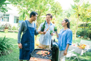 Bir grup Asyalı arkadaş kamp yapıyor ve bahçede akşam yemeği saatinde barbekü yapıyorlar.