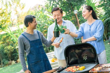 Bir grup Asyalı arkadaş kamp yapıyor ve bahçede akşam yemeği saatinde barbekü yapıyorlar.