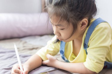 Anaokulu kızı tablet bilgisayar kullanıyor. Rahat bir odada online eğitim alıyor.