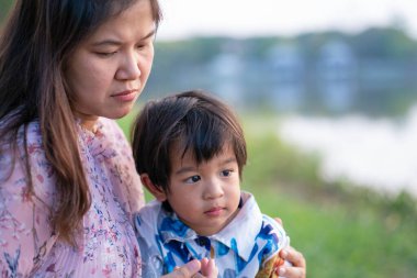 Doğada ağaç parkında rahatlarken annesinin üzerine uzanan sevimli küçük çocuk.