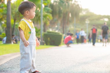 Küçük çocuk hafta sonu tatili için şehir parkında akşam vakti ağaç yemyeşil çimlerde yürüme alıştırması yapıyor.