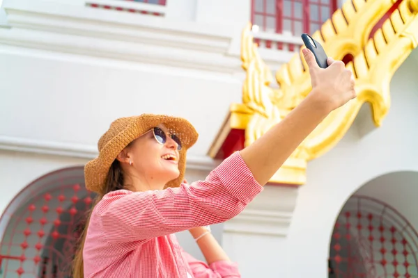 Tourist caucasian foreign backpack  women take selfie photo by smartphone wear sunglass in buddhism temple Bangkok Thailand
