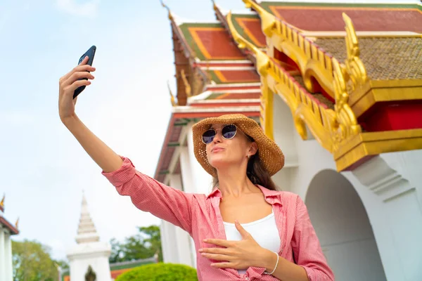 Tourist caucasian foreign backpack  women take selfie photo by smartphone wear sunglass in buddhism temple Bangkok Thailand