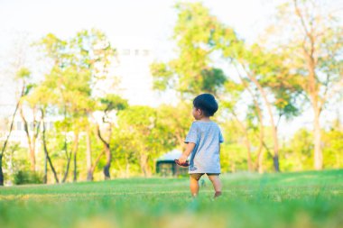 Parkta yeşil çimlerde oynayan sevimli küçük çocuk. Gün batımı doğada hafif çocuk.