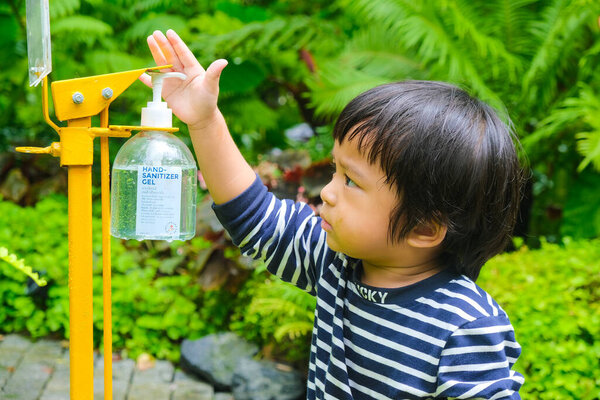 Маленький мальчик с помощью жидкого геля для мытья и чистки рук для предотвращения короны вирус или болезнь Ковид-19 в саду ресторан кафе.
