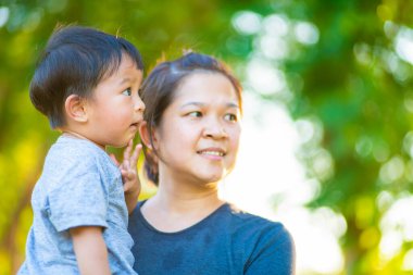 Mutlu çocuk ve annesi yeşil çimlerin üzerinde eğleniyor, annesi parkta yürürken çocuğuna sarılıyor.