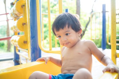 Oyun parkında oynayan küçük çocuk kayganlaştırıcı açık havada eğleniyor.