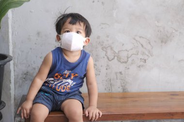 Kafe restoranında maske takan küçük bir çocuk sosyal mesafeli oturuyor.