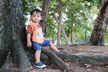 Şehirdeki ağaçta oturan küçük Asyalı çocuk doğadaki halk çocuğu.