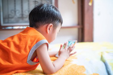 Küçük çocuk evdeki yatakta yatarak internet iletişimi kuruyor.