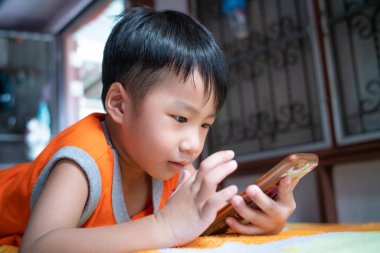 Küçük çocuk evdeki yatakta yatarak internet iletişimi kuruyor.