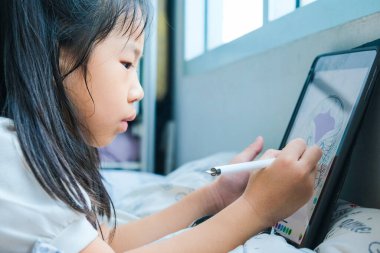 Küçük liseli kız evde çalışan tablet bilgisayarına çizgi film çiziyor.