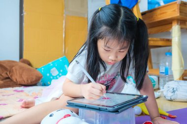 Küçük liseli kız evde çalışan tablet bilgisayarına çizgi film çiziyor.