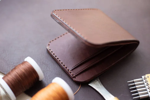 Brown genuine leather men wallet on leather background with craft tool