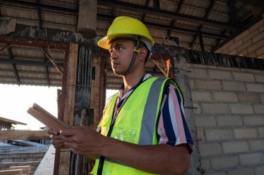Foreman, inşaat alanındaki kayıt verileri için elinde tablet bilgisayar bulunan yeni ev binasını inceliyor.