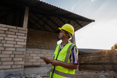 Foreman, inşaat alanındaki kayıt verileri için elinde tablet bilgisayar bulunan yeni ev binasını inceliyor.