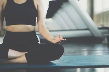 Spor salonunda yoga minderi üzerinde meditasyon yapan Asyalı bir kadın.