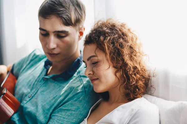 Aşk çifti beyaz odada gitarla eğleniyor Mutlu erkekler ve kadınlar