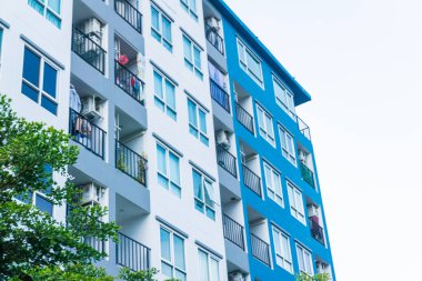 Mavi pencereli, düz ve ev arka planlı modern gayrimenkul apartmanı.