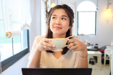 Laptop kullanan ve Latte kahve içen mutlu Asyalı kadın. Restoranda oturan iş kadını.