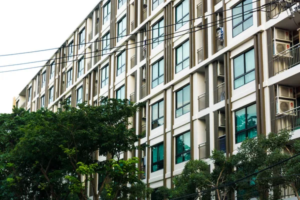 Mavi pencereli, düz ve ev arka planlı modern gayrimenkul apartmanı.