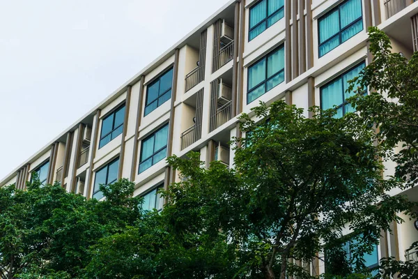 Mavi pencereli, düz ve ev arka planlı modern gayrimenkul apartmanı.