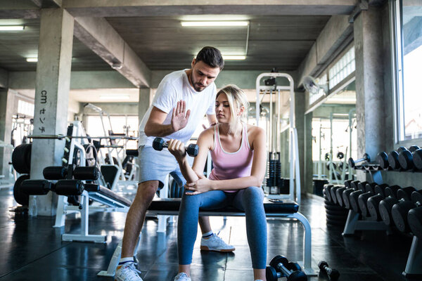 Sport women lifting dumbbell with trainer men in gym body builder