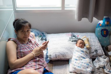 Anne akıllı telefon kullanırken bebek evde uyuyor.