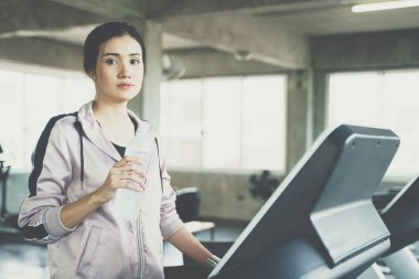 Spor salonunda sağlıklı yaşam tarzında koştuktan sonra Asyalı sporcu kadınlar şişeden su içiyor.