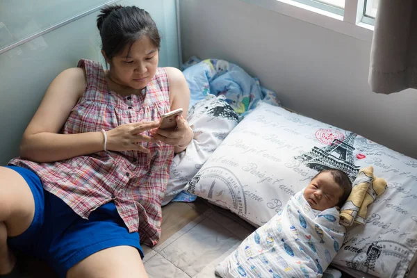 Baby boy sleep in home while mom using smartphone relax time