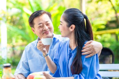 Mutlu Asyalı son sınıf çifti yeşil bahçede kahve içerken mutlu sabahlar.