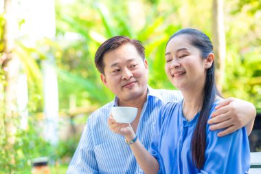 Mutlu Asyalı son sınıf çifti yeşil bahçede kahve içerken mutlu sabahlar.