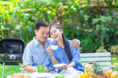 Mutlu Asyalı son sınıf çifti yeşil bahçede kahve içerken mutlu sabahlar.