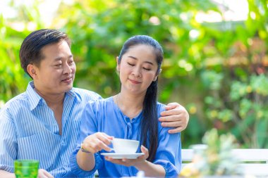 Mutlu Asyalı son sınıf çifti yeşil bahçede kahve içerken mutlu sabahlar.