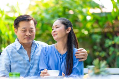 Mutlu Asyalı son sınıf çifti yeşil bahçede kahve içerken mutlu sabahlar.