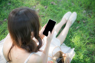 Güzel Asyalı kadın parkta cep telefonu internet bağlantısı kullanarak boş ekran görüntüsü kullanıyor.
