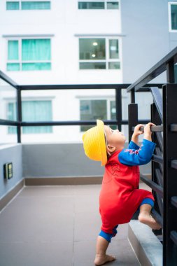 Apartman binasının dışında oynayan küçük çocuk sarı şapka takıyor.