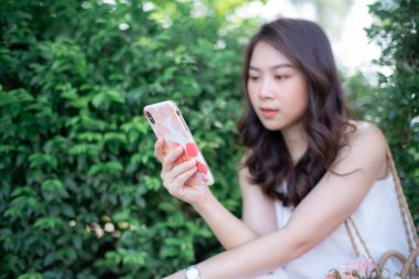 Şehir parkında akıllı telefondan mesaj okuyan gülümseyen güzel bir hippi portresi.