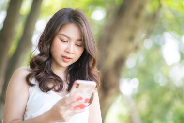 Şehir parkında akıllı telefondan mesaj okuyan gülümseyen güzel bir hippi portresi.