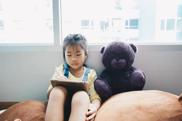 Asian kid girl drawing with tablet computer in cozy house technology education