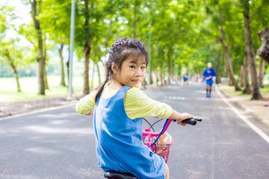 Asyalı kız bisikletle ağaç parkında egzersiz yapıyor.