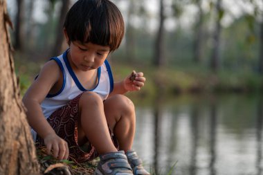 Asian boy sitting under tree sunset time lookimg to the river summer recreation outdoor activity