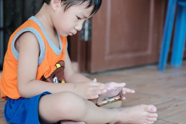 Anaokulu çocuğu akıllı telefonuyla oyun oynuyor. Evinde oturuyor. İnternette oyun oynuyor.