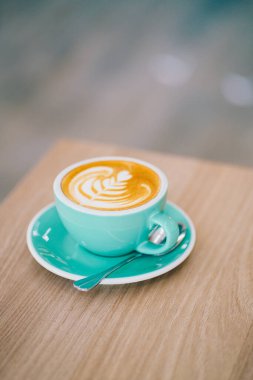 Yeşil seramik bardakta sıcak latte sanatı ahşap masada sanat dokusuyla meşrubat işi yapıyor.