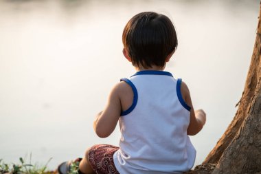 Asian boy sitting under tree sunset time lookimg to the river summer recreation outdoor activity